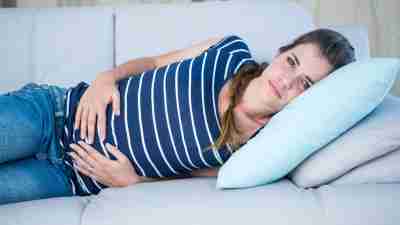 Woman with ADHD laying on couch, holding stomach and suffering from mentrual cramps
