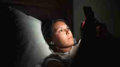 Young woman laying in bed and using smart phone at low light.