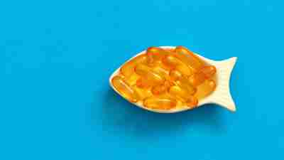 dietary supplement omega in a white bowl in the shape of a fish, vitamins in a bowl like a fish in the sea, fish oil capsules on a blue background, healthy lifestyle concept