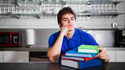 Teen boy with ADHD sitting at kitchen counter with stack of books in front of him staring into space