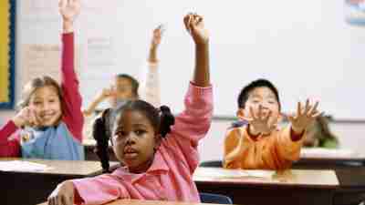 Children raising their hands in a classroom, following the rules for answering a question